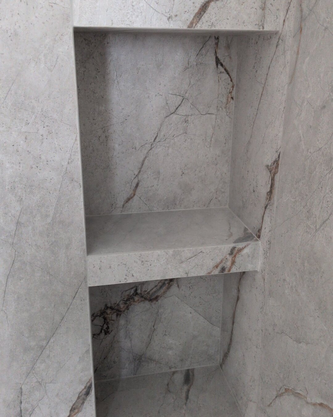 Built-in shower niches in marble-look slab with veining running through the shelves